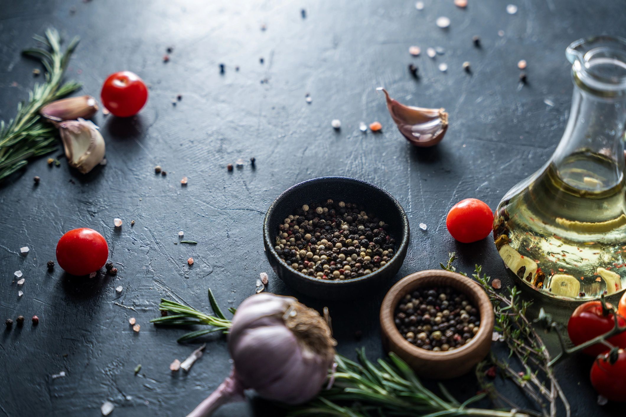 Dunkler Zutaten-Hintergrund mit Öl, Tomaten, Rosmarin und Gewürzen